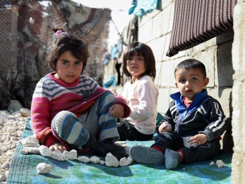 Three children (two girls, one boy) sitting on a woven blanket for a photo.