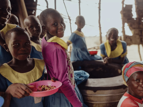 A group of African school children gather while eating school meals and pose for the camera