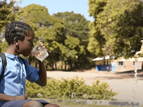 Boy drinks water from a glass outside a school